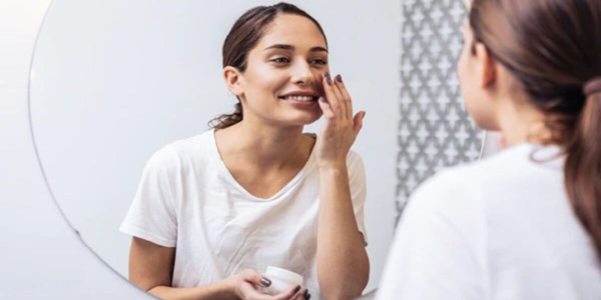 A woman is putting on her makeup in the mirror.