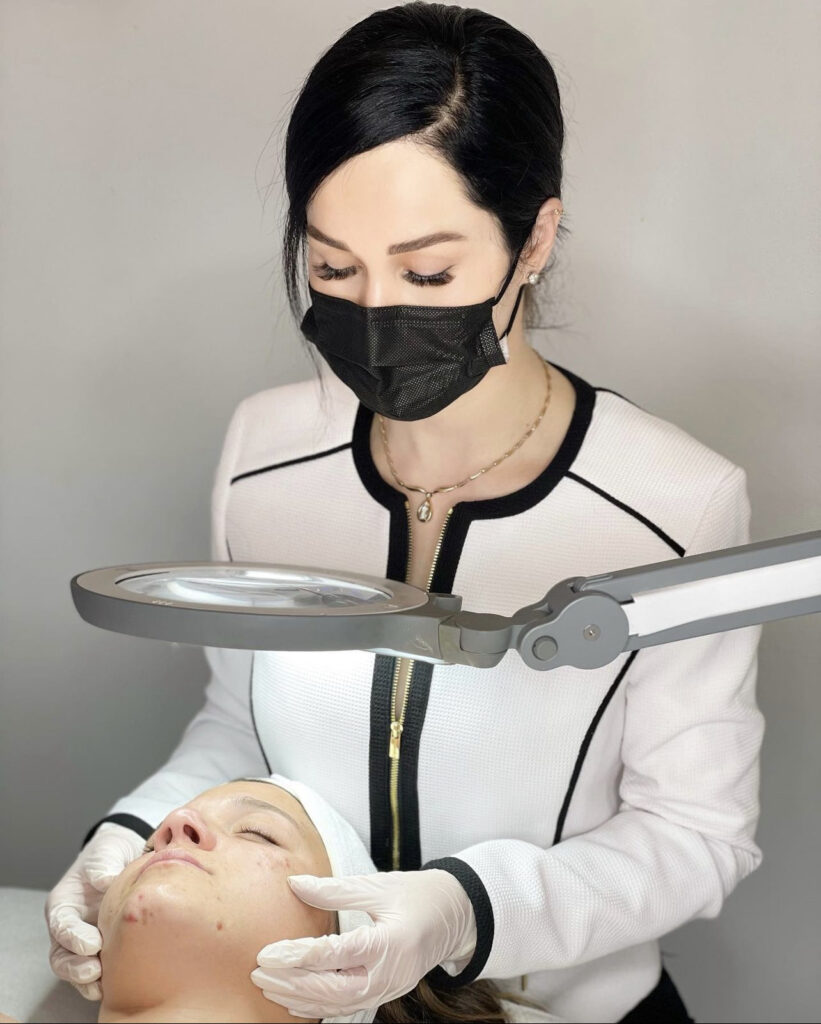 A woman in white shirt and black mask holding magnifying glass.